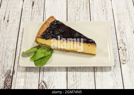 Cheesecake piece with a biscuit bottom and blueberry jam on top on a white plate Stock Photo