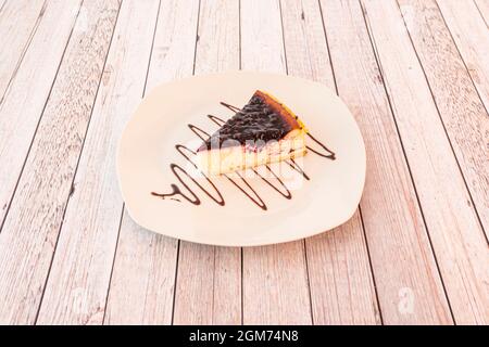 Portion of cheesecake with lots of red fruit jam and garnished with chocolate syrup on a white plate. Stock Photo