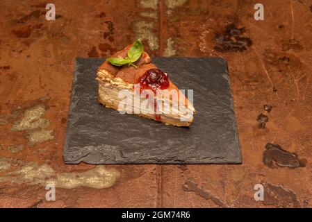 Spectacular portion of cheesecake with strawberry jam that is saying eat me from its black slate plate Stock Photo