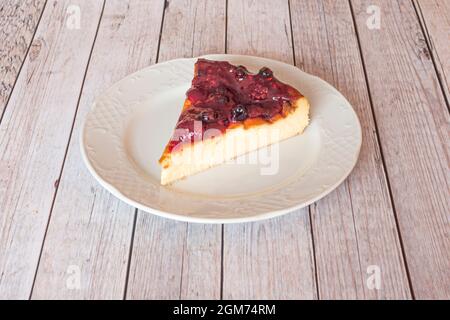 Homemade slice cheese cake with red berry jam and strawberries on top on nice white porcelain plate Stock Photo