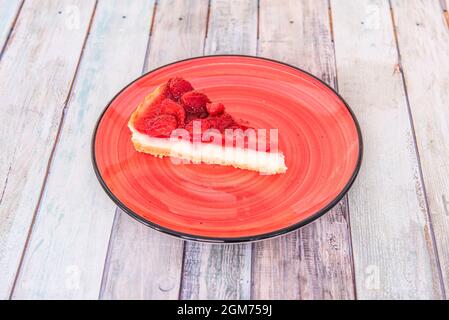 Portion of lemon and strawberry tart on red plate and wooden table Stock Photo