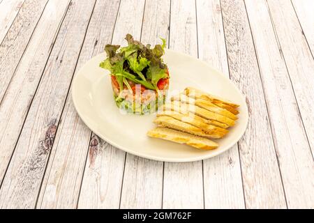 Chopped salmon and avocado tartare, cherry tomatoes, lettuce shoots and toasted bread slices Stock Photo