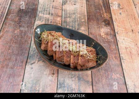 Portion of red tuna tataki with sprouted soybean sprout on a blue bowl and a meat table Stock Photo