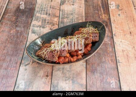 Asian recipe for red tuna tataki with diced tomato and bean sprouts in a dark bowl on a wooden table Stock Photo