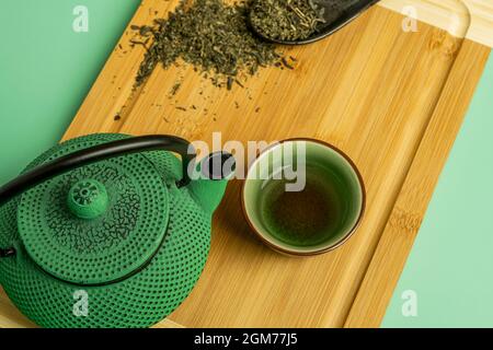 Closeup of green cast iron teapot with green porcelain cup with tea and bamboo wood table Stock Photo