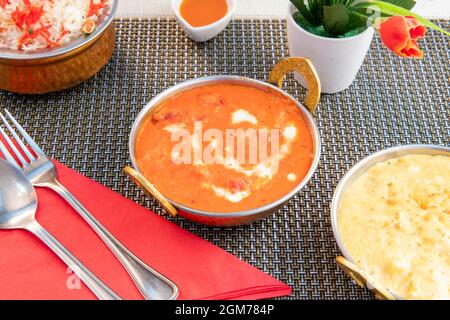 Chicken tikka masala curry on gray tablecloth, topped with red napkin and pilau rice garnish. Stock Photo