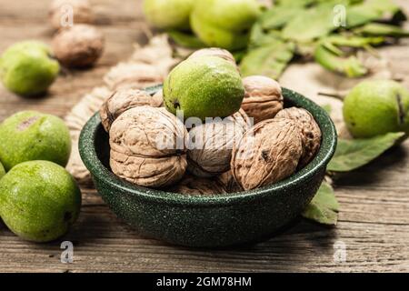 Ripe brown and unripe green walnuts in a bowl. Old wooden background, close up Stock Photo