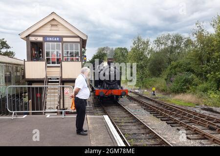 Steam train UK - steam locomotive approaching Ongar Station, with signal box and stationmaster in attendance, Epping-Ongar Heritage Railway Essex UK Stock Photo