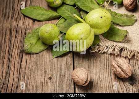 Ripe brown and unripe green walnuts on sackcloth napkin. Old wooden background, copy space Stock Photo