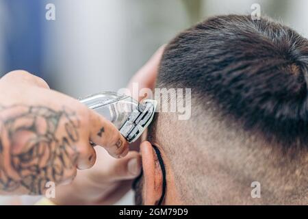 Tattooed hand using a shaving machine to cut hair of a costumer in a barber shop Stock Photo