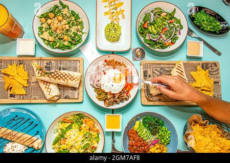 set of salads from around the world, wrap with corn nachos, salmon poke bowl, fried meat and cheese sauce, wakame seaweed salad, spinach and avocado s Stock Photo