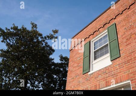 A corner window with wood green shutters of an old red brick garden apartment building during a sunny afternoon. In Arlington, Virginia near Washingto Stock Photo