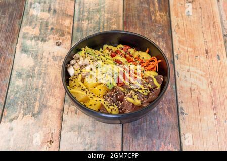 Poke bowl of red tuna fuji with mango, pieces of mushrooms, ripe avocado and salad of cherry tomatoes, carrots and white rice base Stock Photo