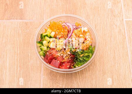 Poke bowl of red tuna, shrimp, sunflower seeds and seeds, wakame salad, carrot zest, red onion, cucumber in pieces and white rice in take away contain Stock Photo