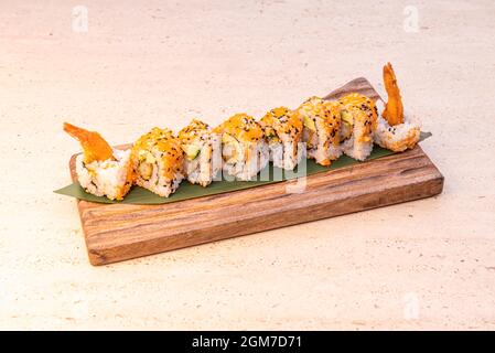 Uramaki dragon roll stuffed with fried gabardine prawns and orange fish roe and avocado on banana leaf Stock Photo