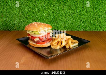 Pork burger with cheese, piquillo peppers, tomato slices, white onion rings, iceberg lettuce and a portion of French fries Stock Photo