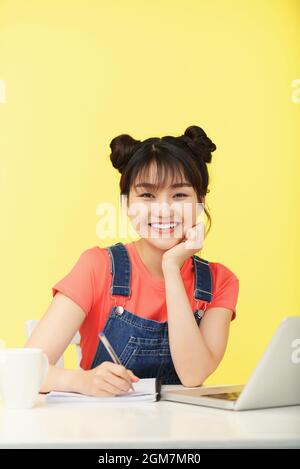 Portrait of happy young woman with beautiful toothy smile writing essay in copybook at her desk Stock Photo