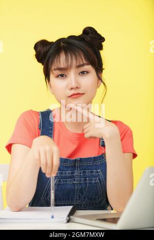 Portrait of pretty bored young woman pointing at copybook with pen and looking at camera Stock Photo