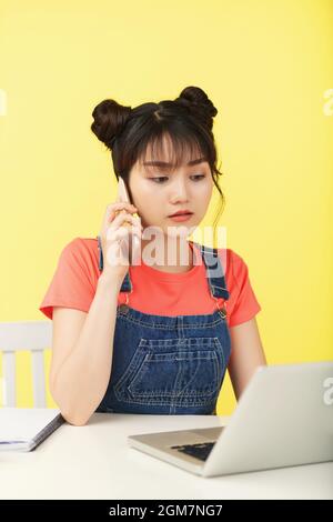 Serious female college student talking on phone with fellow student and doing homework on laptop Stock Photo
