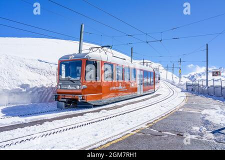 RIFFELBERG, SWITZERLAND - APRIL 13, 2018: The Matterhorn Gotthard Bahn also known as the Gornergrat train. Bright red locomotive contrasts with deep b Stock Photo