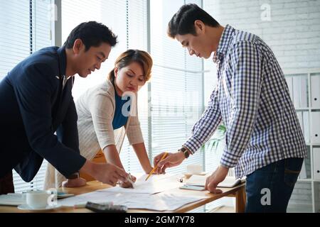 Team of serious business people bending over office table when discussing many charts and documents with marketing statistics Stock Photo