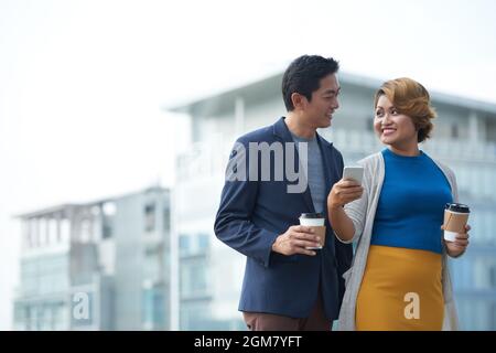 Cheerful mature business colleagues discussing funny meme about office workers on social media when drinking coffee outdoors during break Stock Photo