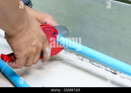 Using a cutter for plastic pipes in the repair of household water supply, plumbing hand close-up. Stock Photo