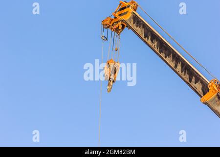 Yellow truck crane boom with hooks for lifting containers and the use of weight overboard above blue sky Stock Photo