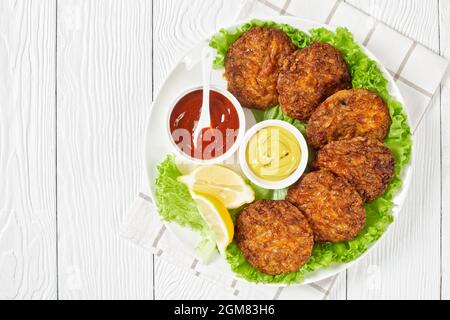 baked pork patties with cheese crust on a green lettuce lives with ketchup and mustard on a plate, flat lay, free space Stock Photo