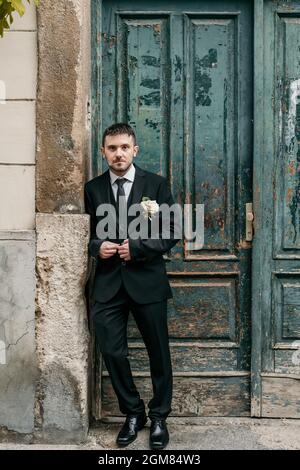 Portrait of groom standing in front of old green wooden door on wedding day. Stock Photo