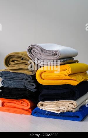 Bobbins with threads, measuring tape and stack of colorful fabrics on table. Tailoring accessories Stock Photo