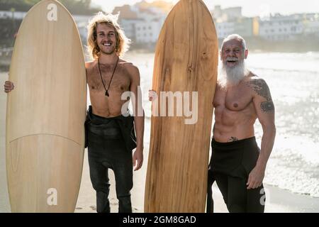 Happy fit surfers with different age surfing together at sunset time - Extreme sport lifestyle and friendship concept Stock Photo