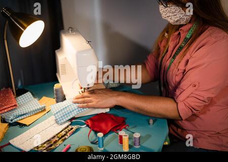 Hispanic woman working with sewing machine doing homemade face mask for preventing and stop corona virus spreading Stock Photo