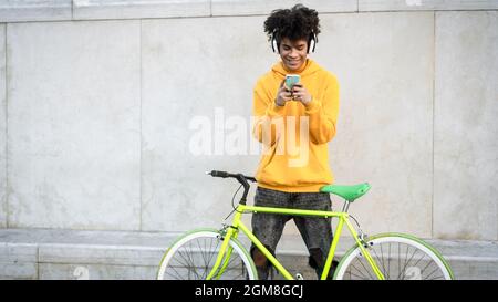 Happy African man using mobile smartphone outdoor while riding with bike in the city - Youth millennial generation lifestyle and technology concept Stock Photo