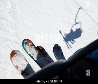 two pairs of skis, people on the lift climb the snow-covered mountain slope. cold winter sunny day. active rest, sports hobbies. Shadow from skiers Stock Photo