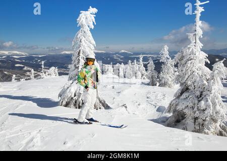 teenage girl in a bright ski suit in a good mood is skiing on a beautiful snow-covered mountain slope on a cold winter sunny day. Interesting active w Stock Photo