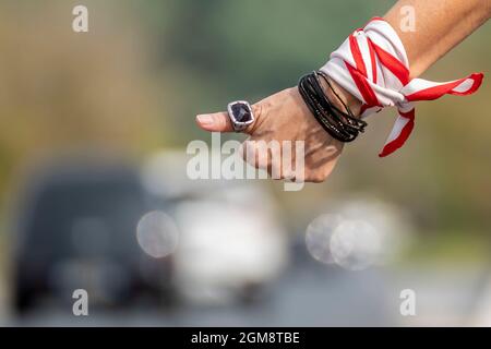 A female hand makes the classic gesture of hitchhiking along a busy road Stock Photo