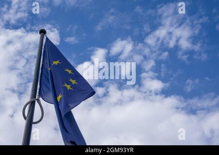 European Union flag on blue sky with white clouds background with copy space. EU flag flying in front of cloudy blue sky. Flag of european union waving and space for text. Blue flag with 12 stars Stock Photo