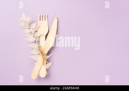 Wooden cutlery, fork and takeaway knife with a dry branch of a flower on lavender background. Stock Photo