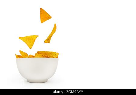 Tortilla corn chips are falling into a white ceramic bowl on a white background with place for text. Stock Photo