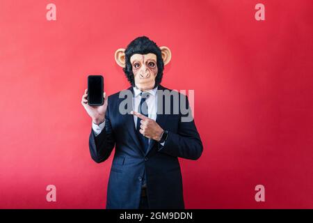 Businessman wearing monkey mask and showing a smartphone. Stock Photo