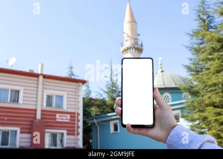 Mockup image of woman hand holding white desktop screen mobile phone. Blurry mosque view in the background. Stock Photo
