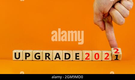Symbol of planning 2022 upgrade new year. Businessman turns a wooden cube and changes words 'upgrade 2021' to 'upgrade 2022'. Beautiful orange backgro Stock Photo