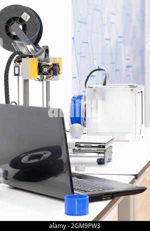 3D printers, rolls of 3D PLA filament, laptop and 3D printed plastic parts on a white table. Stock Photo