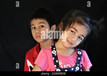 The brother standing behind his sister, they are making fun and spending the time very joyfully together. face expression Adorable little girl and boy Stock Photo