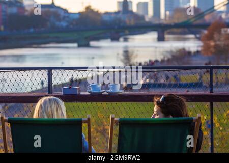 Two woman dinking coffee and sitting on the rooftop of restaurant Oosten, looking over the park and promenade at River Main, in the background the sky Stock Photo