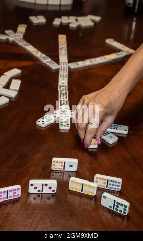 A game of chicken claw dominos with a hand playing a tile and showing one persons game pieces with reflections in wooden table Stock Photo