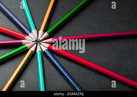 Wooden pencils of different colors in the shape of a star on a black background. Top view Stock Photo
