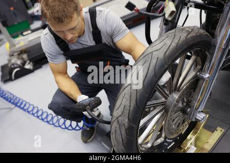 Man repairman inflating motorcycle tires in auto repair shop Stock Photo