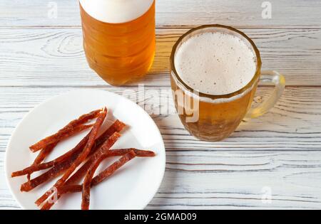 Beer is poured from a plastic bottle into a glass mug and slices of dried fish on a white plate Stock Photo